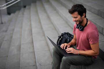 Handsome man working with laptop on city street. Man using his laptop while sitting on stairs outdoors.