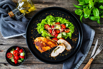 Stuffed chicken breast with mozzarella and fresh vegetable salad on wooden background
