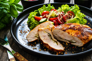 Stuffed chicken breast with mozzarella and fresh vegetable salad on wooden background
