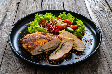 Stuffed chicken breast with mozzarella and fresh vegetable salad on wooden background
