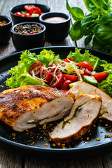 Stuffed chicken breast with mozzarella and fresh vegetable salad on wooden background
