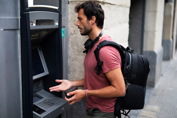 Young man withdrawing money from credit card. Man typing pin code on keypad of ATM machine.