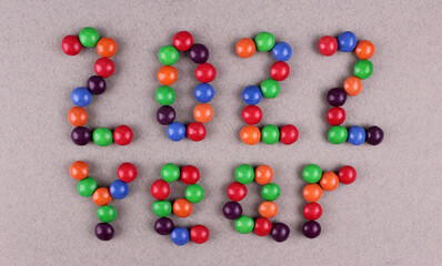 Inscription ''2022 year'' from multi-colored round sweets on a gray background