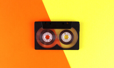 Black audio cassette on a yellow-orange background