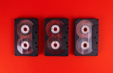 Three black audio cassettes on a red background. Retro technology