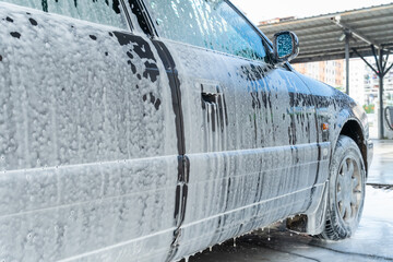 Gray car in white foam at a self-service car wash
