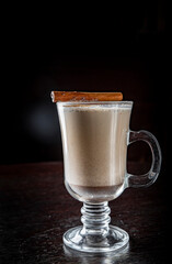 traditional Christmas drink Eggnog with cinnamon, anise, vanilla sticks on rustic wooden table on dark background