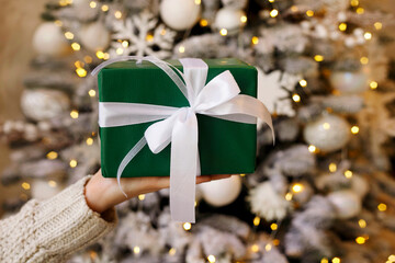 Close up woman hand with green eco gift box over christmas tree lights background. Christmas holidays, present, happiness concept
