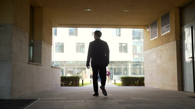silhouette of business asian man rear back view goes down the corridor in the arch in the modern office center. outside. successful confident businessman walk go to the building through tunnel