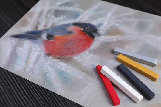 Colorful chalk pastels and beautiful painting of bullfinch on black wooden table