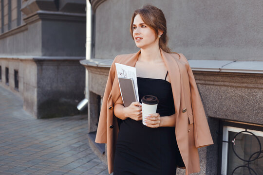 Businesswoman with coffee to go, digital tablet and documents walking street in morning.