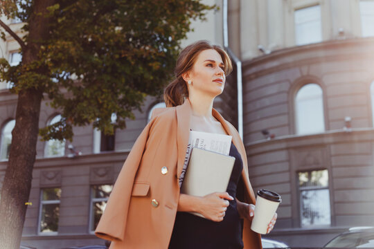 Businesswoman with coffee to go, digital tablet and documents walking street in morning - Powered by Adobe