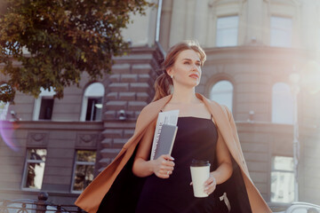 Businesswoman with coffee to go, digital tablet and documents walking street in morning