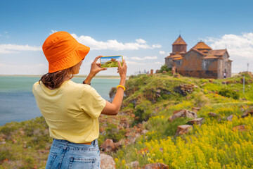 Happy woman tourist taking pictures of a famous Armenian Hayravank Monastery and Sevan Lake. Travel...