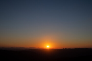 bright sun disappearing behind the mountain in the late afternoon at sunset