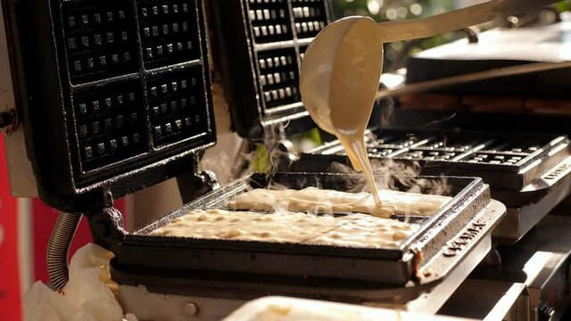 Close-up chef pours waffle batter in a waffle iron in a professional kitchen. Waffle making at the hotel with all-inclusive meals.