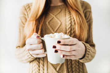 Beautiful woman with red hair hold in her hands mug with hot coffee with whipped cream, marshmallow and cinnamon