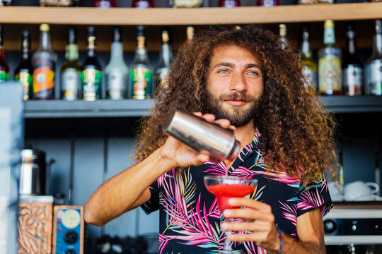 Handsome smiling curly hair bartender preparing cocktail at the resort bar - Powered by Adobe
