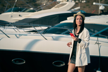 young woman strolling through a marina, with smartphone and boats behind