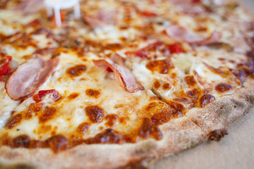 Tasty fresh Pizza with ham, yellow cheese, pepper, and vegetables on а cardboard plate. Selected focus.