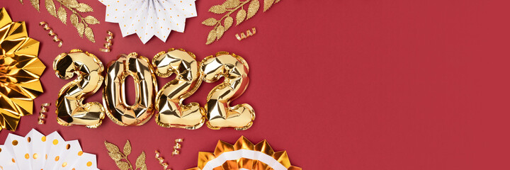 Banner with 2022 inflatable golden balloons and glittering  decorations on a red background. New Year's concept.