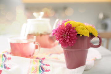 Beautiful bright flowers in pink cup, fabric and aromatic tea on table indoors, space for text