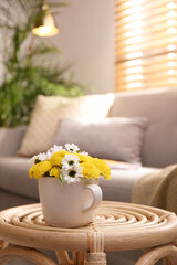 Fototapeta na wymiar Cup with beautiful bright flowers on table in living room