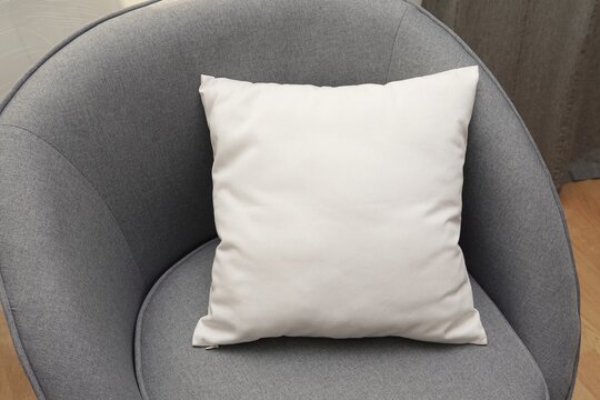 White square canvas pillow mockup on grey armchair, small cotton cushion mockup in living room interior.