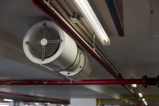 Fan In Modern Building Parking In Door. Parking Building Ventilation System. Blower Flow Air For Confined Space Work In Factory. Industrial Fan Heater And Cooler.