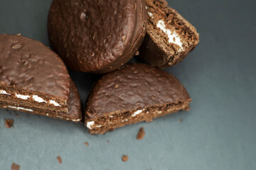 Cookies in chocolate glaze and white cream filling scattered on a dark background. Top view.