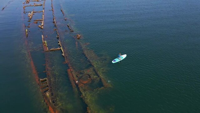 Aerial shot. Young women is having fun. Stand Up Paddling in the sea. SUP. Paddling among debrees of a sunk metal ships