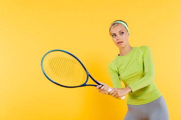 young woman in green long sleeve t-shirt playing tennis isolated on yellow