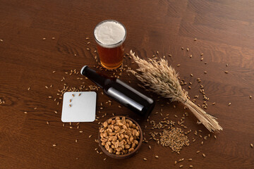 Blank beer bottle and glass with beer, peanuts bowl, wheat, malts, beer pad, on a wooden background, craft beer mockup templates, with empty space to place your label or design