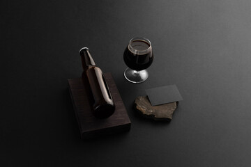 Beer bottle on a wooden block with business card and glass on the black background, craft beer...