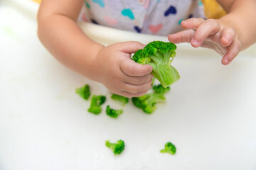 Baby eats pieces of broccoli vegetables. Selective focus.