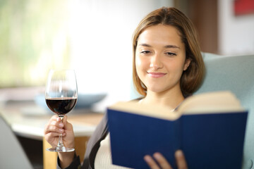 Happy woman reading a book drinking wine on a couch
