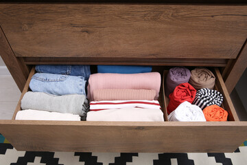 Open drawer with folded clothes indoors. Vertical storage of clothing