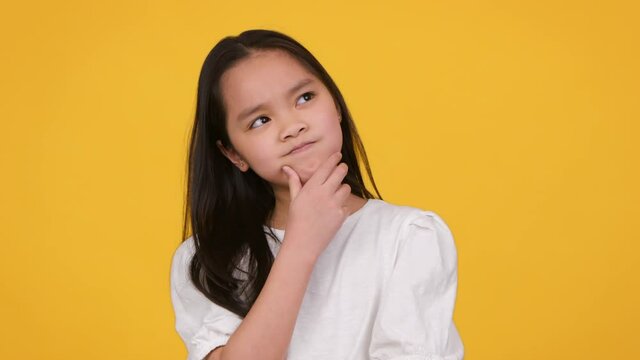 Hmm, Let's Think. Studio Portrait Of Cute Thoughtful Little Asian Girl Contempaining About Idea, Touching Her Chin