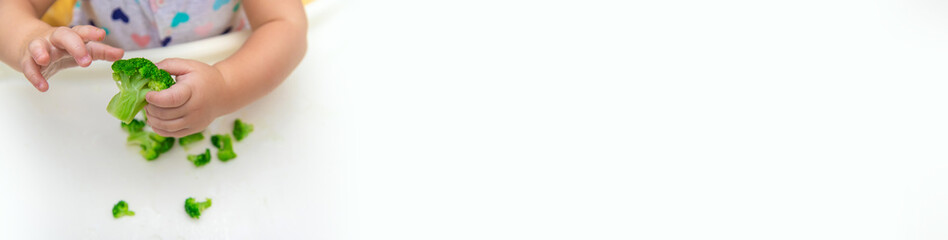 Baby eats pieces of broccoli vegetables. Selective focus.