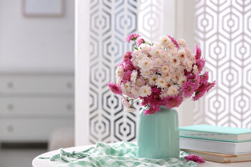 Vase with beautiful bouquet, books and checkered cloth on white table in room. Space for text