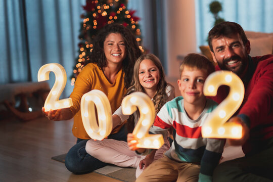 Parents and children holding illuminative numbers 2022 while celebrating New Year