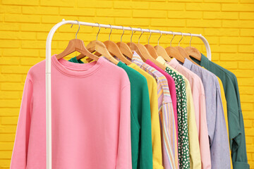 Rack with stylish clothes near yellow brick wall