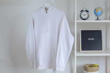 Mockup of white hoodie hanging on metal hanger with decorations on iron rack isolated on white...