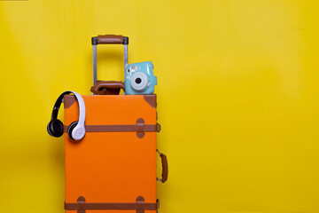 Orange suitcase with wireless headphone and mini camera isolated on yellow background for travel concept with minimal style