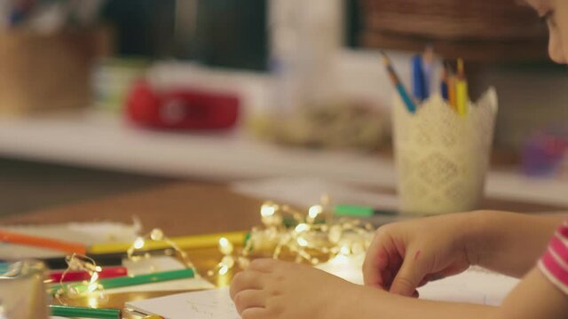 On the eve of the new year at home, a mother draws Christmas drawings with a cute son of preschool age, who glues stickers in the form of a santa claus.
