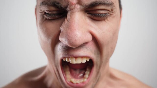 Close-up portrait of a angry man with crooked teeth yelling wide open his mouth on a white background. 