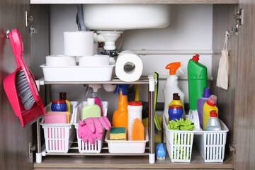 Open under sink cabinet with different cleaning supplies in kitchen - obrazy, fototapety, plakaty