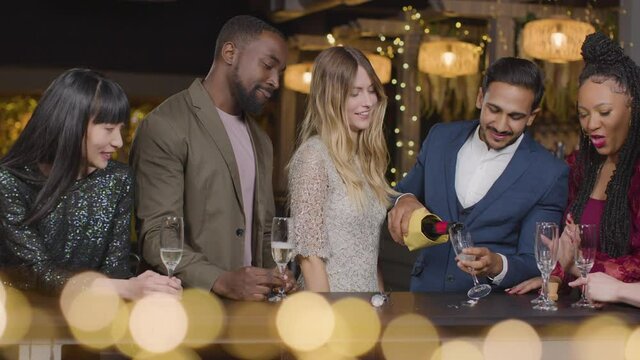 Sliding Shot of Friends Pouring Champagne During New Years Celebrations In a Bar