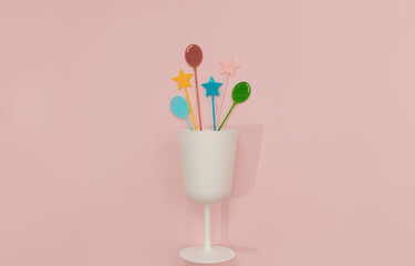 White matte glass with splashes of colourful cocktail cupcake picks on pastel pink background. Minimal Happy birthday flat lay. Celebration card or party concept. Holiday idea.