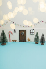 Mini elf or mouse house diy toy gift for kids made with tiny door, window with lantern and Christmas green tree of pipe brushes. Little bulb garland on white wall. Holiday decor on blue background.